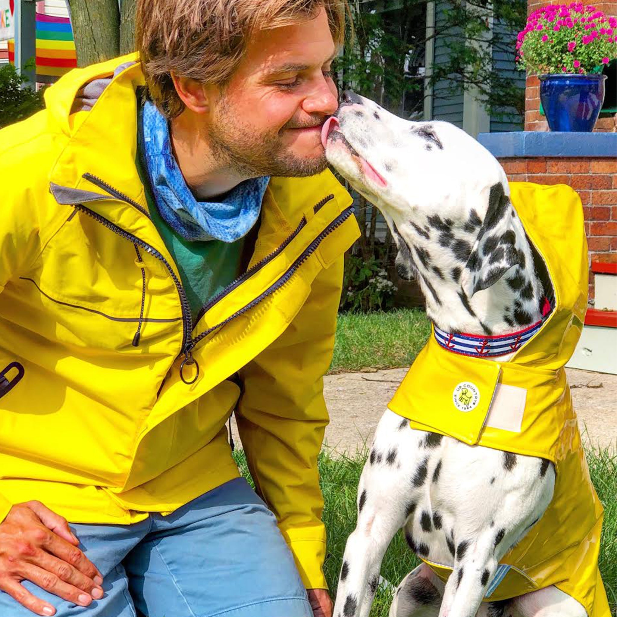Man in a yellow raincoat with a Dalmatian dog also in a yellow raincoat, outdoors. dog kisses