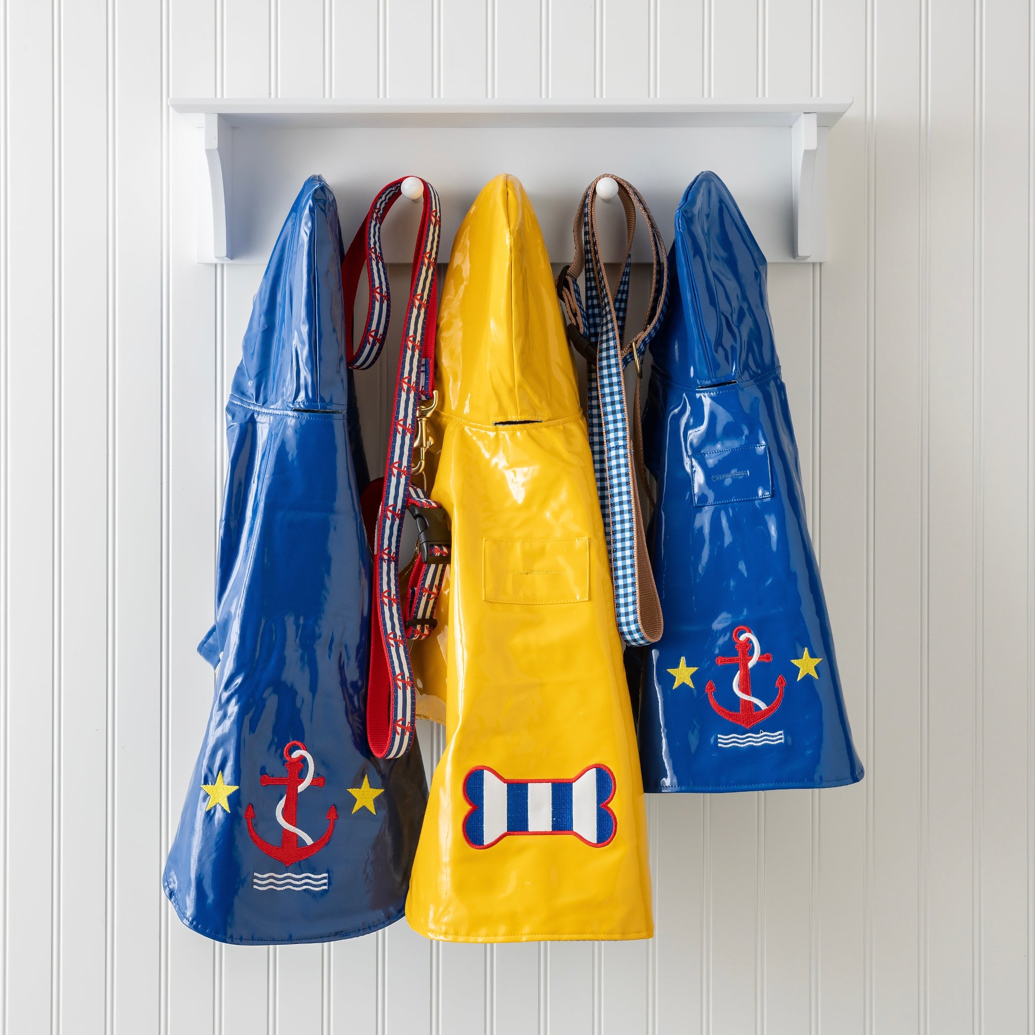Four colorful raincoats with anchor and bone designs hanging on a white wall.